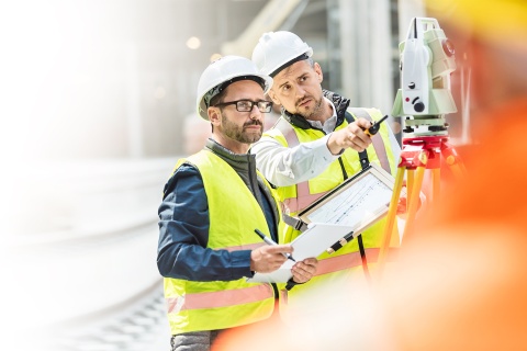 Zwei Männer mit Warnweste und Schutzhelm an der Arbeit als Ingenieure - helle Farben