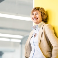 Frau im Blazer lehnt lächelnd an einer Wand - bunte Farben